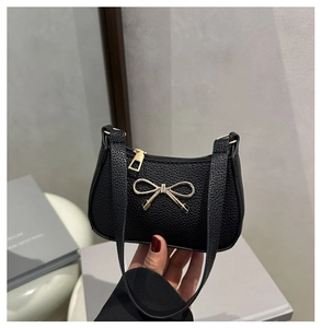 Détail de la texture cuir noir et du nœud doré décoratif sur le sac à main de luxe