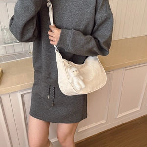 White crescent dumpling crossbody bag with a plush bear charm and adjustable strap