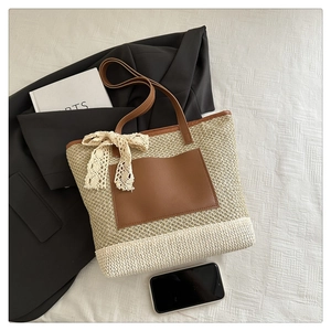 Detail of woven straw tote bag with brown faux leather pocket and lace bow on bed linen