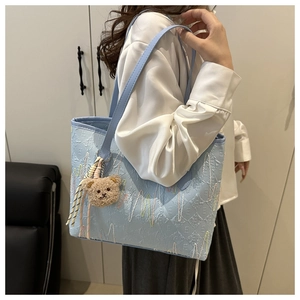 Detail of light blue tote bag with embossed texture and cute brown teddy bear charm