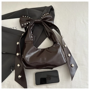 Detail of dark brown glossy bag featuring oversized bow handle with silver rivets
