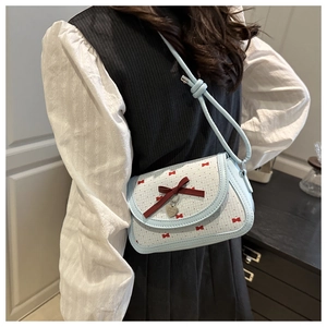 Détail du sac à bandoulière bleu clair avec nœud rouge et pendentif cœur sur un modèle