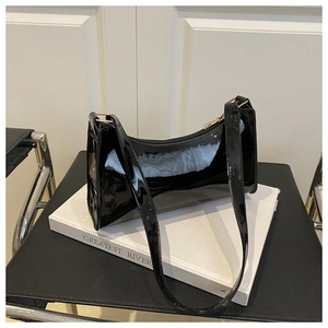 Glossy black patent leather underarm bag with gold zipper detail on a white book
