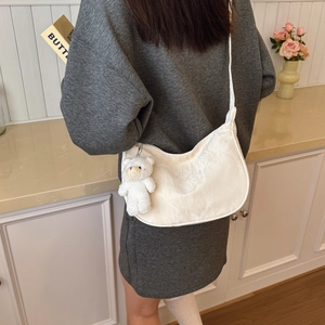 White dumpling-style crossbody bag with plush bear charm worn by a model in a cozy setting