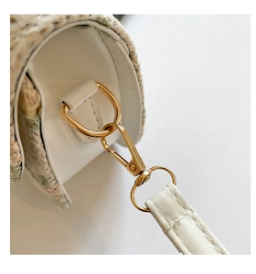 Detail of light gold lobster clasp and white lychee grain leather strap on woven saddle bag