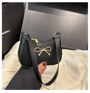 Détail du sac en cuir grainé noir avec un ornement de nœud doré et une fermeture éclair chic