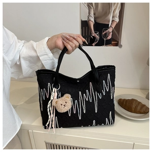 Detail of black tote bag featuring wave embroidery and a cute plush bear charm