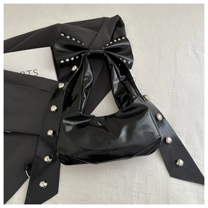 Close-up of black glossy shoulder bag with bow detail and silver stud accents