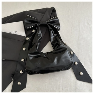 Detail of glossy black patent leather bag featuring oversized bow and silver rivet studs