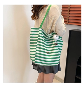 Detailed side view of a green striped canvas tote bag with a white plush doll charm accessory