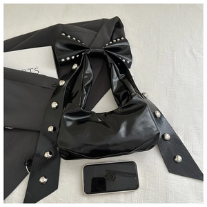 Close-up of black glossy faux leather bag with bow detail and silver metal studs