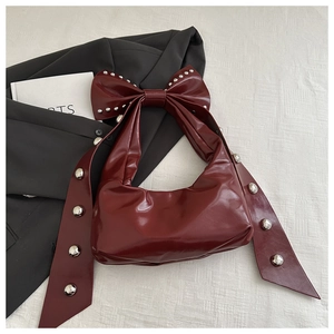 Detail of burgundy patent leather tote bag with oversized bow and silver rivets