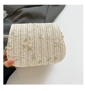 Close-up of woven straw saddle bag featuring delicate floral embroidery and green leaves