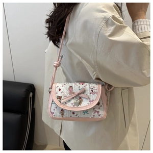 Détail d'un petit sac bandoulière beige et rose avec motifs de dessins animés et pendentif