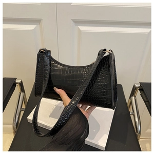 Detail of a vintage black crocodile pattern shoulder bag held by a model in a modern room