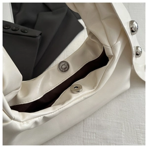 Detail of cream white shoulder bag featuring magnetic buckle closure and silver rivets