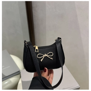 Détail de la texture grainée noire et du nœud doré sur un sac porté à l'épaule