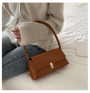 Sac baguette marron avec boucle dorée porté par un mannequin en tenue de maille chic