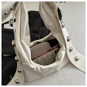Detail of off-white shoulder bag with large silver studs on wide strap and spacious interior