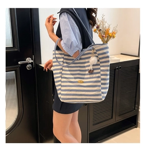 Dettaglio della borsa tote in tela a righe bianche e blu con placca dorata e ciondolo peluche