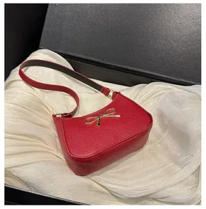 Détail du sac rouge en cuir grainé avec boucle nœud dorée sur doublure en soie blanche