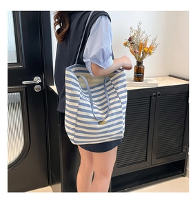 Detalle del bolso tote de lona a rayas azules y blancas con placa de logo metálica