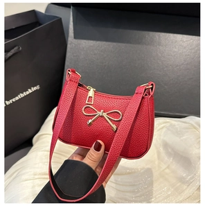 Détail du mini sac en cuir grainé rouge avec nœud en métal doré et fermeture éclair