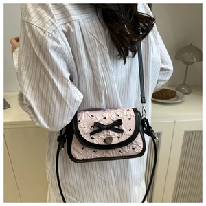 Détail du sac bandoulière rose avec pendentif cœur porté par un mannequin en intérieur