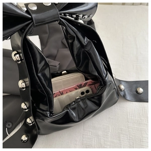 Detail view of black rivet shoulder bag with bow handle showing interior capacity