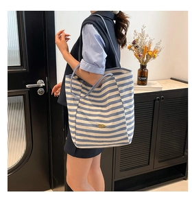 Detail of blue and white striped canvas tote bag showing metal logo and texture