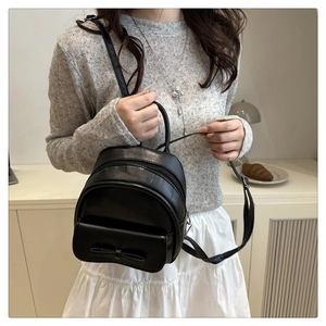 Detail of a black mini backpack with a bow accent worn by a model in a casual setting
