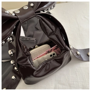 Detail of dark brown glossy bag with oversized rivet bow and spacious interior