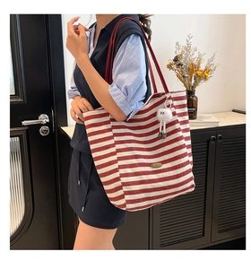 Detailaufnahme der rot gestreiften Canvas-Tasche mit Trageriemen und Plüsch-Anhänger