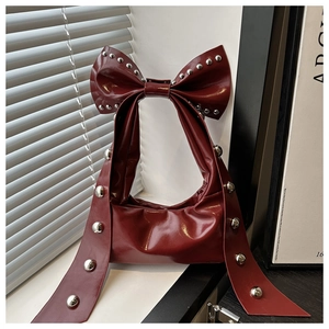 Detailed view of dark red patent leather bag featuring silver rivets and bow handle
