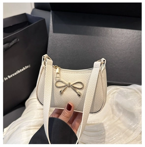 Détail du sac beige texture litchi avec nœud doré sur fond de soie élégante et raffinée
