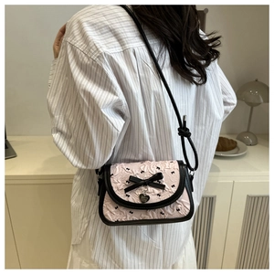 Détail du sac bandoulière rose à motif nœud et pendentif cœur porté par un modèle