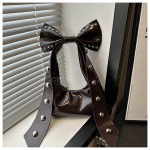Detail of dark brown glossy patent leather bag with silver rivets and large bow decoration