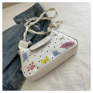 Close-up of cream polka dot tote bag with cartoon patches and thin shoulder strap
