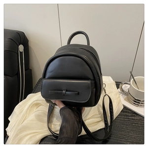Detail of a mini black faux leather backpack with a bow held by hand to show compact size