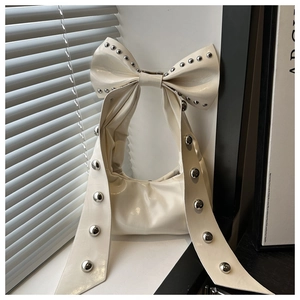 Detail of cream patent leather handbag featuring bow handle and silver rivet studs