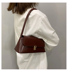 Détail d'un sac baguette marron foncé vintage avec boucle dorée sur fond de manche blanc