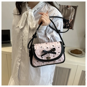 Sac bandoulière floral avec nœud en soie et pendentif cœur tenu par un modèle