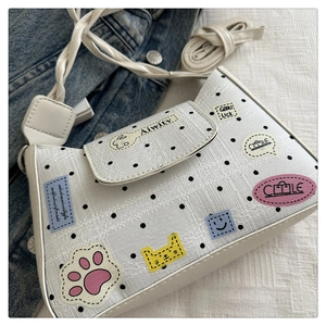 Close-up of white polka dot crossbody bag with colorful cartoon patches on denim fabric