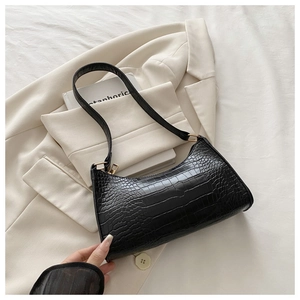 Detailed close-up of a black croc-embossed baguette bag on a white suit background