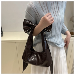 Detail of dark brown patent leather shoulder bag featuring silver rivets and bow accent