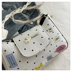 Detail of white polka dot crossbody bag with cartoon patches and woven strap