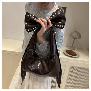 Close-up of dark brown leather underarm bag with oversized bow and silver studs detail