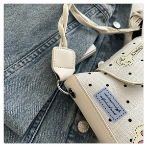 Close-up of white polka dot tote bag with woven shoulder strap and silver metal buckle