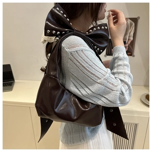 Detail of dark brown bow-shaped shoulder bag with silver rivet studs and glossy finish