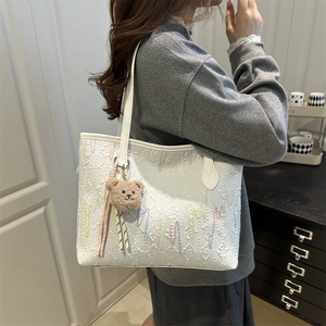 White embroidered tote bag with color wave patterns and a brown plush bear charm